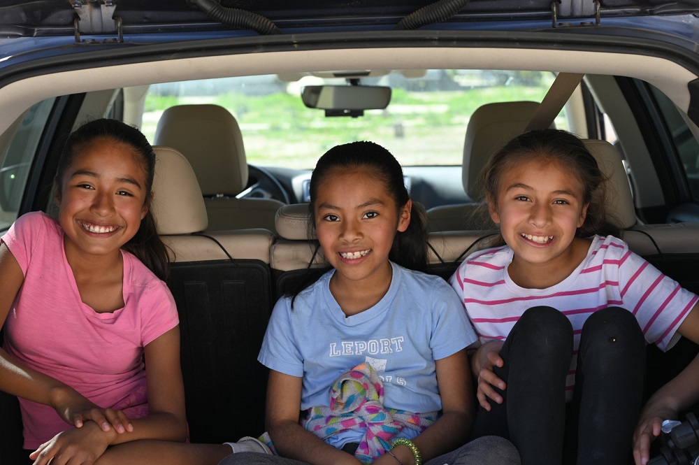three young girls are sitting back side of a suv